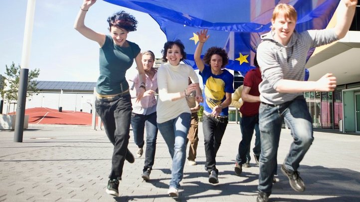 Junge Menschen laufen unter einer großen EU-Flagge in einem Schulhof