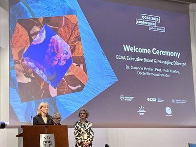 3 Frauen auf Bühne bei Eröffnungszeremonie mit Präsentation im Hintergrund