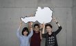 3 international students hold an Austria cut-out in the air.