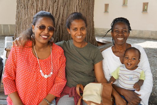 the scholarship holders from Africa and one little baby boy sitting on a bench and smiling to the camer