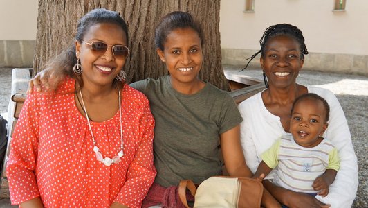 the scholarship holders from Africa and one little baby boy sitting on a bench and smiling to the camer