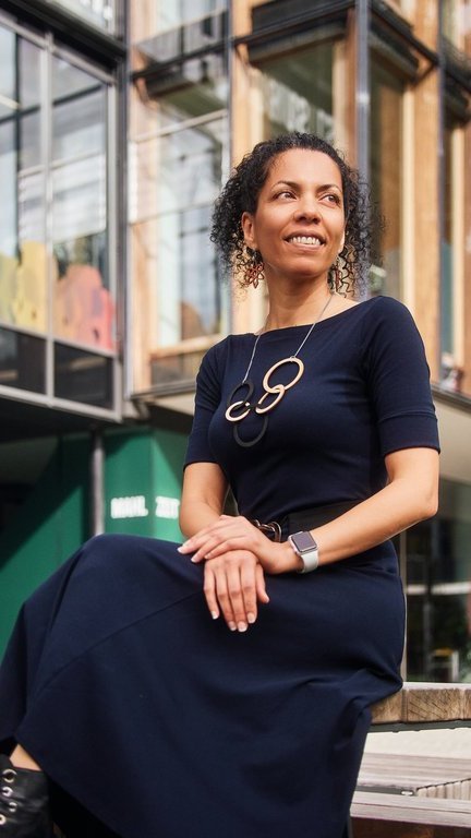 Eine Frau schaut in die Ferne, hinter ihr ein modernes verglastes Gebäude