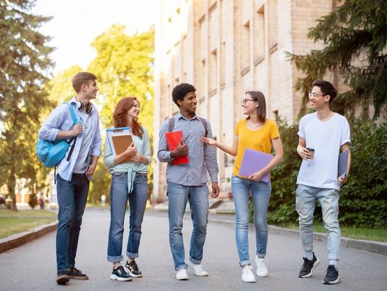 Cheerful multicultural college classmates walking together after study, discussing their plans, full length