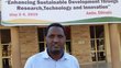 Geda Oncho standing in front of Ambo University, with a big poster in the background