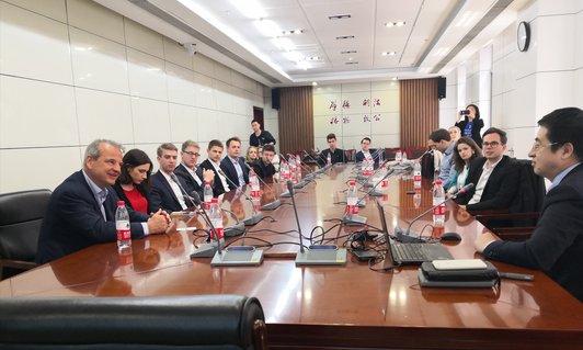 Meeting room with a very large table and people sitting around, each with a microphone and a water bottle in front of them.