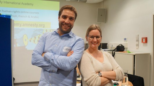 A man and a woman standing with folded arms and laughing