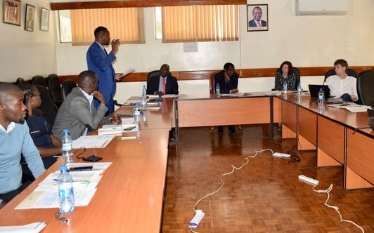 people sitting around tables arranged in U-shape, one person standing and talking