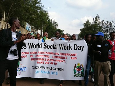 Gorup of people with a big white flag with information on the 28. World Social Work Day on it walking on the streets