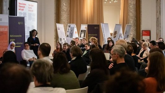 Podiumsdiskussion beim hdgö (Haus der Geschichte Österreichs). Blick aus dem Publikum heraus. Im Hintergrund sind mehrere Roll-ups mit Information zu sehen.