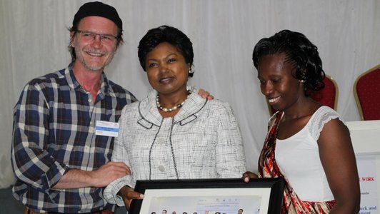 Three people posing for a photo while holding a picture of a group photo in their hands