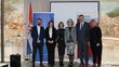 Six adults pose for a picture with the flag of the canton of Western Herzegovina and an OeAD roll-up behind them