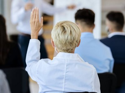 back view of businesswoman attending a seminar and raising her arm to ask a question.