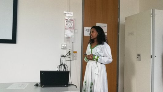 A woman standing in front of the door in a room, a laptop is at the table in front of her