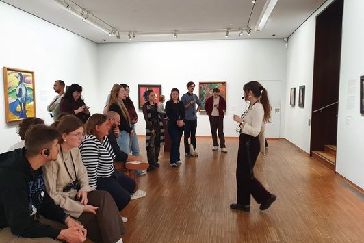 Mehrere Menschen in einem Raum mit weißen Wänden, an denen Bilder hängen (im Museum)