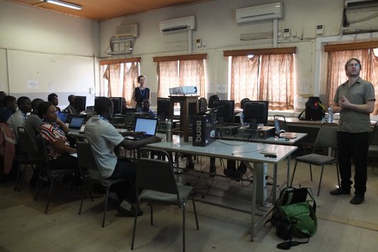 Group of people sitting at their workplaces and look at a man standing in front of them