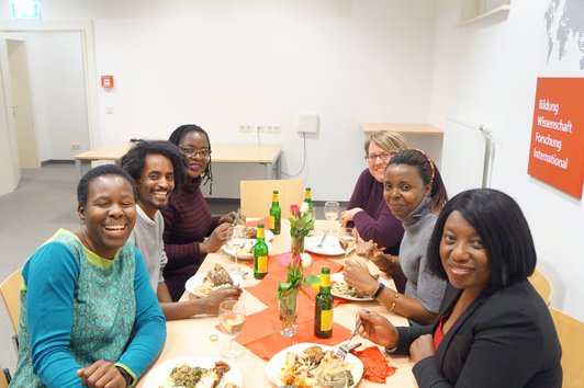 Six people sitting at a table, eating and drinking and smiling.