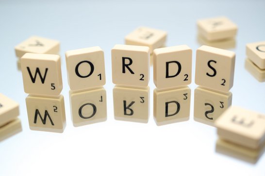 Das Wort: "Words" in scrabble Bausteinen wurde auf einer Spiegelnden Oberfläche aufgestellt. Ein paar lose Steine liegen drumherum.