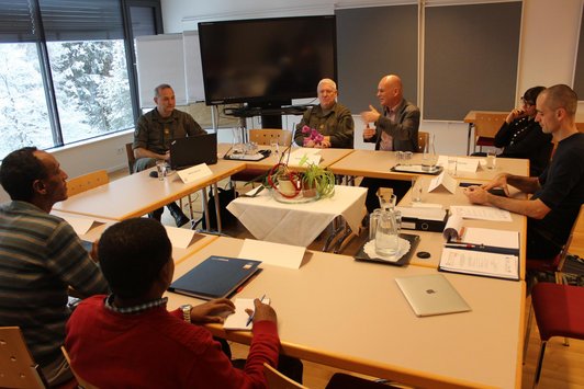 Group of people sitting around tables and one man is talking