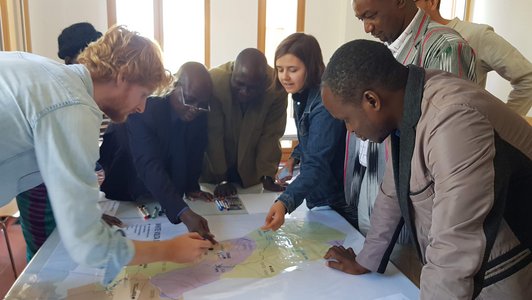 Group of people standing around a table and looking and pointing at a map 