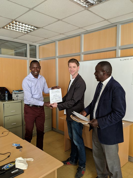Three smiling man standing together, showing a piece of paper into the camera