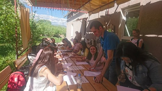 Group of people sitting at a big table outdoors and one guy is standing