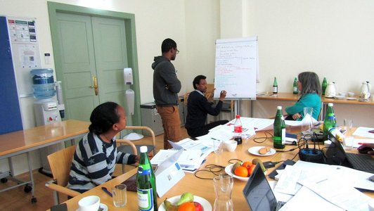 One person writing on a flip chart, three other persons looking at him.