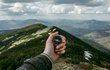 Hand, die einen Kompass hält. Im Hintergrund Berge und Wolken