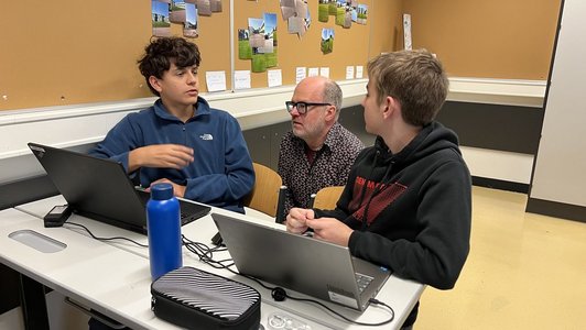 Wissenschaftsbotschafter mit zwei Schülern bei der Arbeit an Laptops im Gymnasium Neusiedl