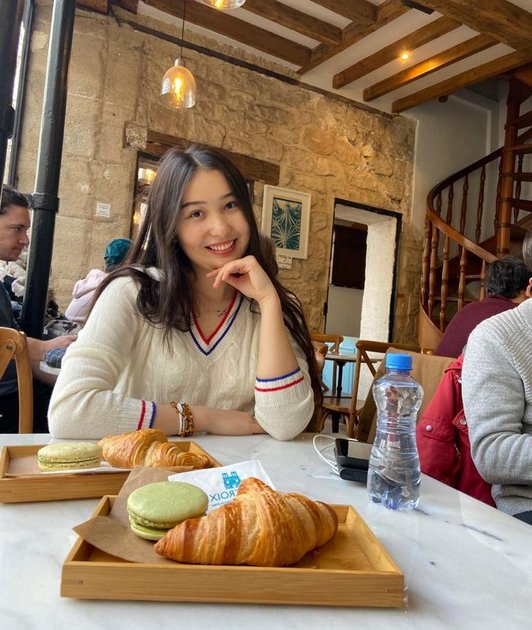 Aimen Azamatkyzy in a coffeehouse. infront of her there is a plate with a croissant. 