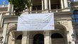 Das Haupttor des Hauptgebäudes der Universität Wien. Es ist ein großes Banner aufgespannt, welches einen schönen internationalen DeutschlererInnen Tag wünscht.