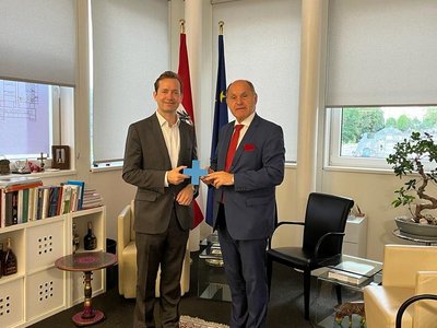  The managing director of the OeAD meets with Wolfgang Sobotka in an office. They hold up a blue cross together.