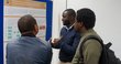 Three men standing in front of a poster of the poster presentation discussing its content