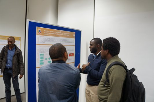 Three men standing in front of a poster of the poster presentation discussing its content