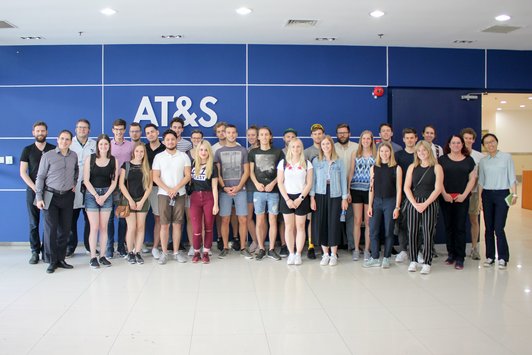 Group of students standing in front of a blue wall with the inscription "AT&S" and looking into the camera