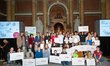 A large group of students who won the Citizen Science Awards in the ballroom of the University of Vienna. The students hold up checks with the prize money.