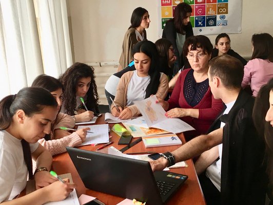 Group of people sitting together at a table writing something while looking at a notebookscreen