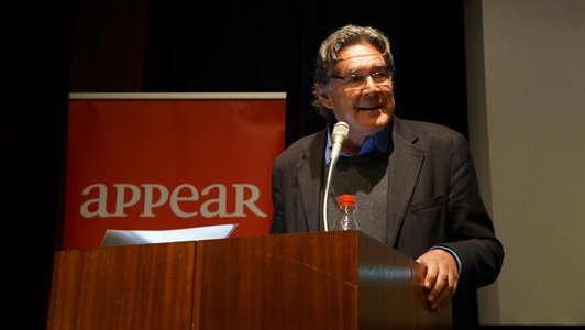 The picture shows Andreas Obrecht as he is giving a speech at a speaker's desk. There is a roll-up reading "appear" in the background.