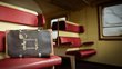  A worn suitcase in an old train compartment with red seats.