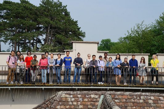 Many students from all over the world standing next to each other in the Laxenburg part area and smiling to the camera