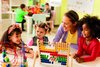 Eine Kindergärtnerin sitzt mit drei Kindergartenkindern an einem Tisch