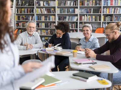 Bürger:innen bei Citizen-Science-Aktivität an Schreibtischen vor großem Bürcherregal