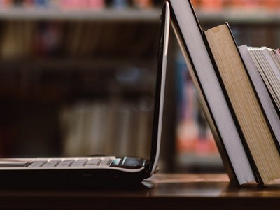 Laptop aufgeklappt und Bücher vor Bücherregal