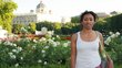 Kasha Tadel Gebre, in a white T-shirt, stands in front of a park with white flowers and a magnificent building in the background. 