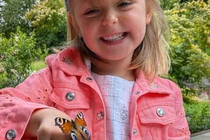 Lächelndes Mädchen mit einem Schmetterling auf ihrer rechten Hand