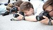 Four photographers lying on the ground to take a photo. Everyone looks through their camera.