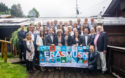 Zahlreiche Männer und Frauen posieren für das Gruppenfoto beim OeAD-Retreat und halten ein Plakat von Erasmus+.