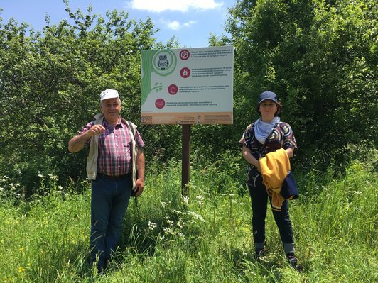 A man and a woman standing next to an informaton sign in the midst of green landscape