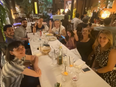 Gruppe an acht Personen sitzt gemeinsam in einem Restaurant an einem Tisch und lacht in die Kamera