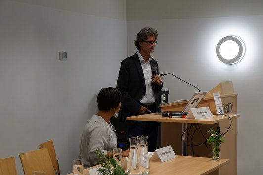 Man standing behind a desk presenting the project and woman sitting next to him
