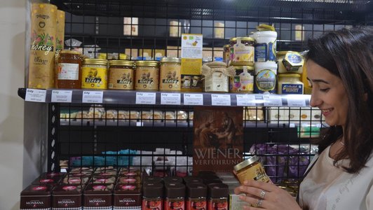 Women in a supermarket next to a shelf holding a glass of honey in her hands